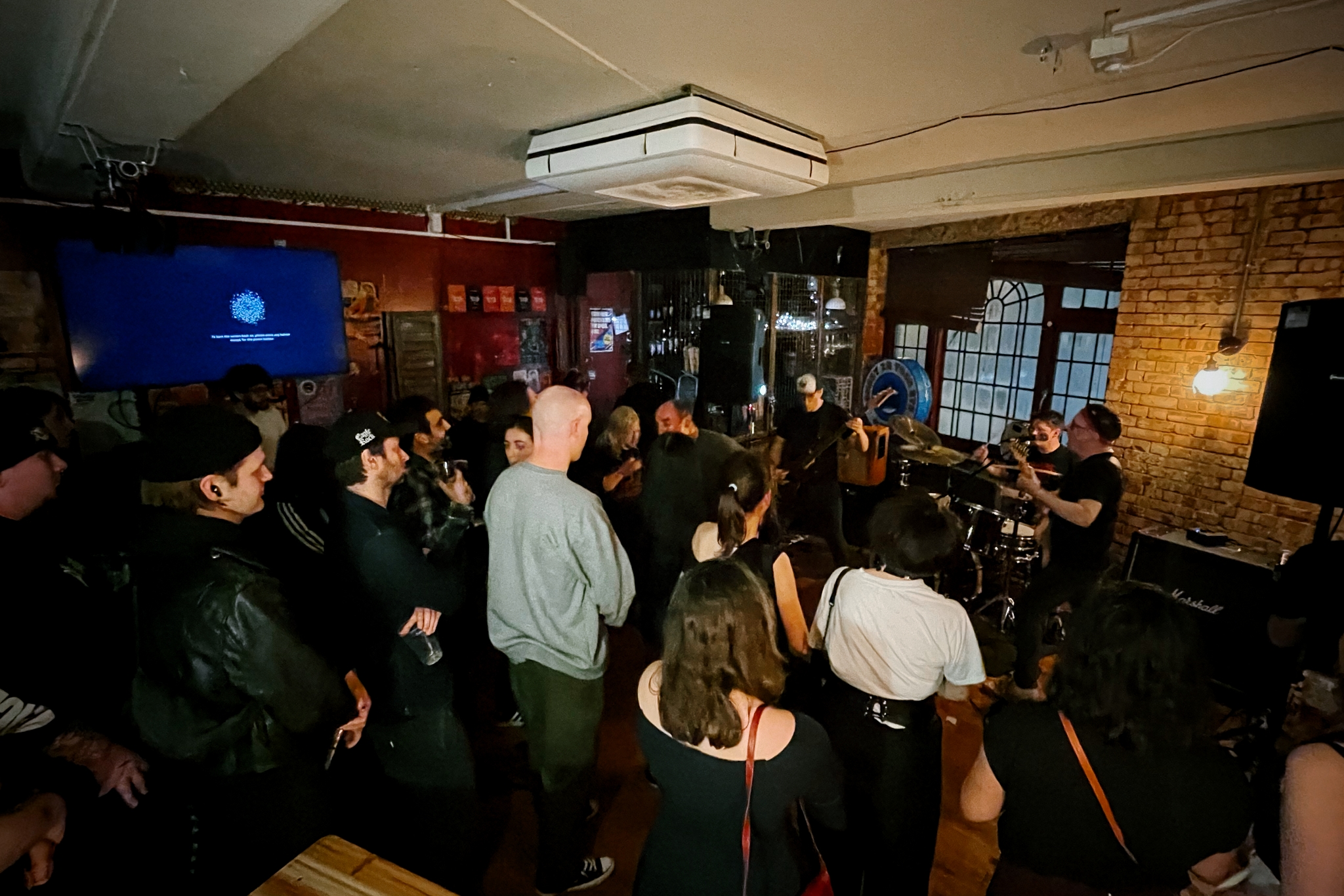 Photograph of a tiny venue taken from behind the audience who are standing watching a band play.
